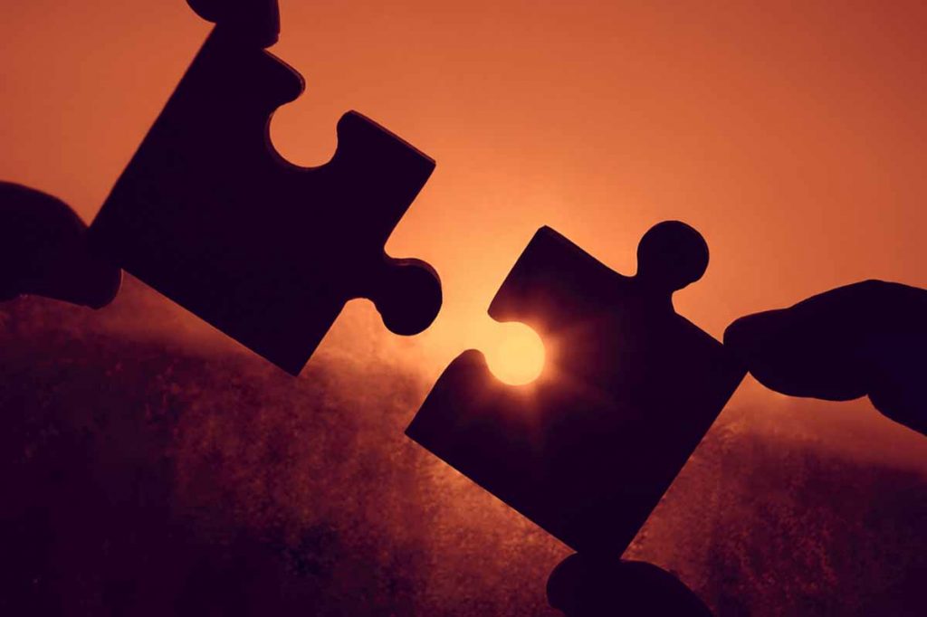 Puzzle pieces held apart in front of sun glare.