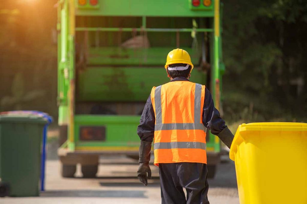Recycling collection worker taking bin to truck. 